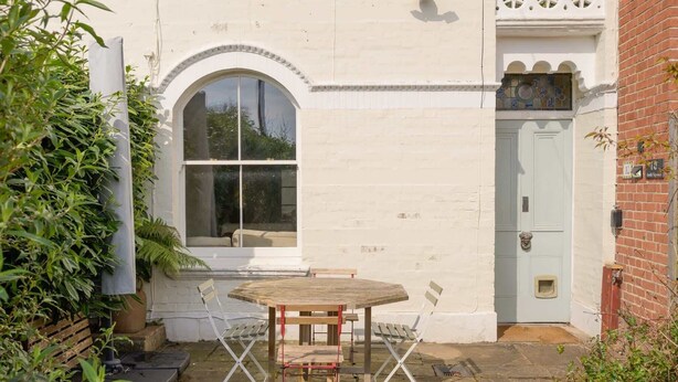 A small patio with a table and chairs, a window, and a door. - Colourful Victorian Home in Redland with Garden (Bristol City)