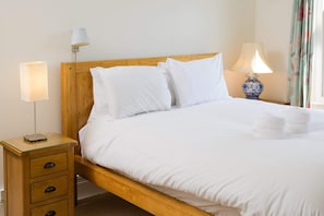 A neatly made bed with white linens, a wooden headboard, a bedside table with a lamp, and a blue vase.