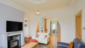 A living room with a fireplace, a television, a sofa, and a coffee table. - Colourful Victorian Home in Redland with Garden (Bristol City)