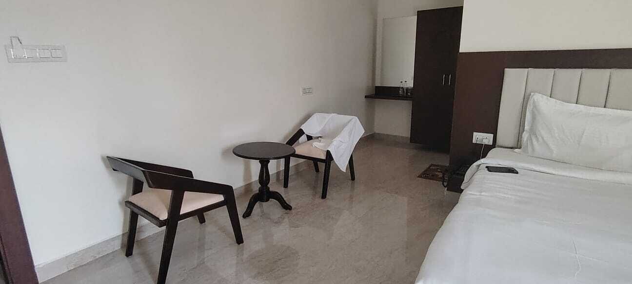 A hotel room with a bed, a chair, a small table, and a mirror.