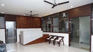 Un área de recepción moderna con mostrador de mármol, paneles de madera y puerta de vidrio con la letra 'A' satinada.