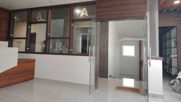 Un área de recepción con un escritorio de madera, una puerta de vidrio de acceso y un felpudo con la palabra 'Welcome'.