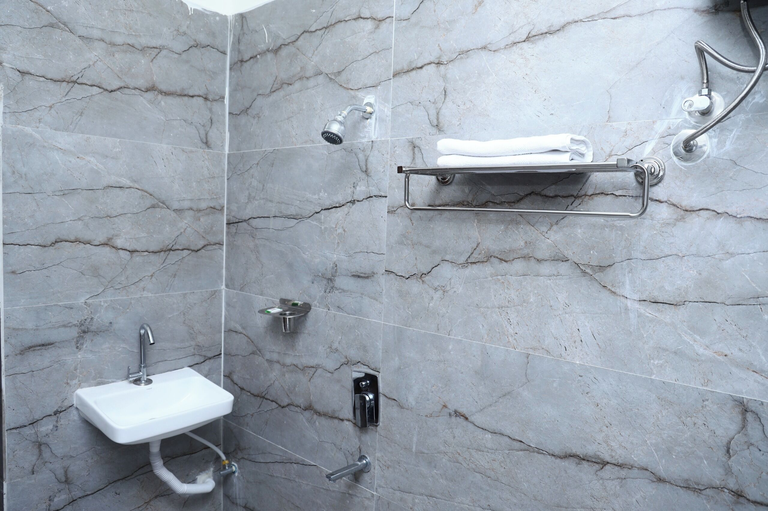 A bathroom with a marble wall, a white sink, a towel rack, and a shower.