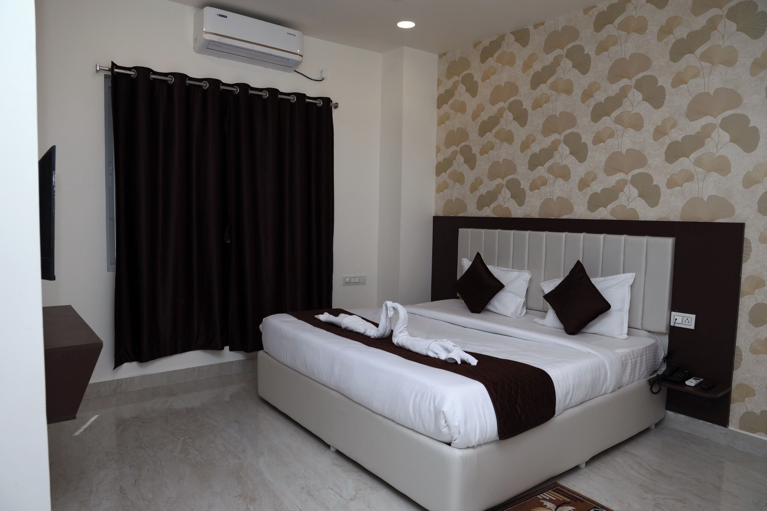 Een hotelkamer met een groot bed, een flatscreen televisie, een wandairconditioner en behang met een patroon.