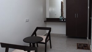 Un pasillo con dos sillas de madera, una mesita pequeña, un armario de madera oscura y un espejo en la pared.