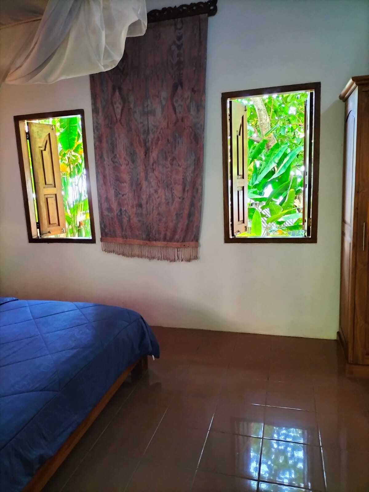 A room with a bed, two windows with views of greenery, a curtain, and a wooden wardrobe.