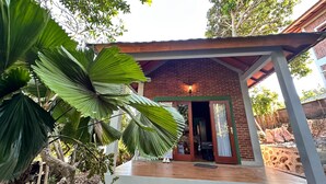 A brick building with a wooden porch and a large green plant in the foreground. - Villa Kamila Senggigi By Villaloka (Senggigi)