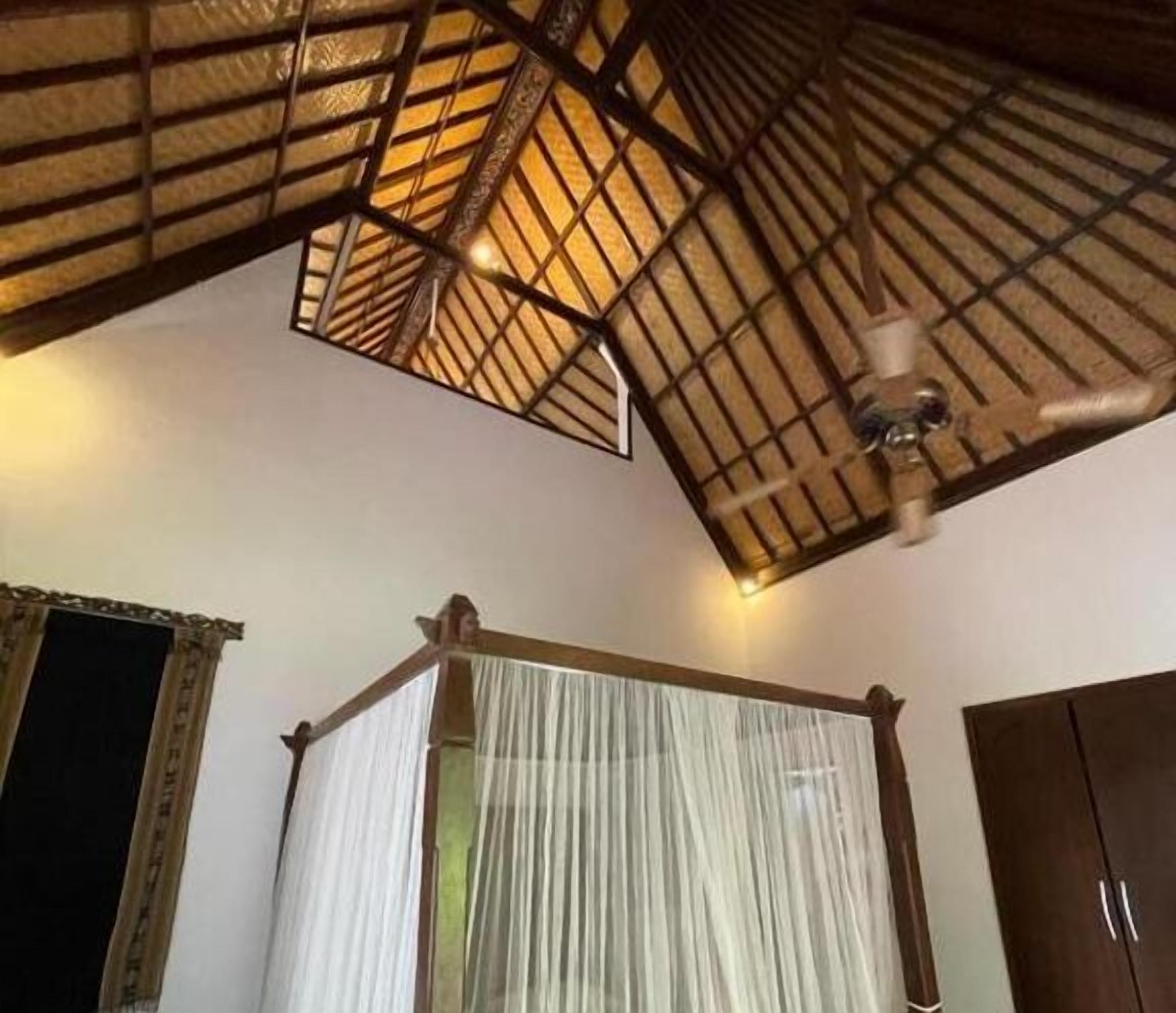 A room with a high ceiling, a bed with a canopy, and a wooden ceiling structure.