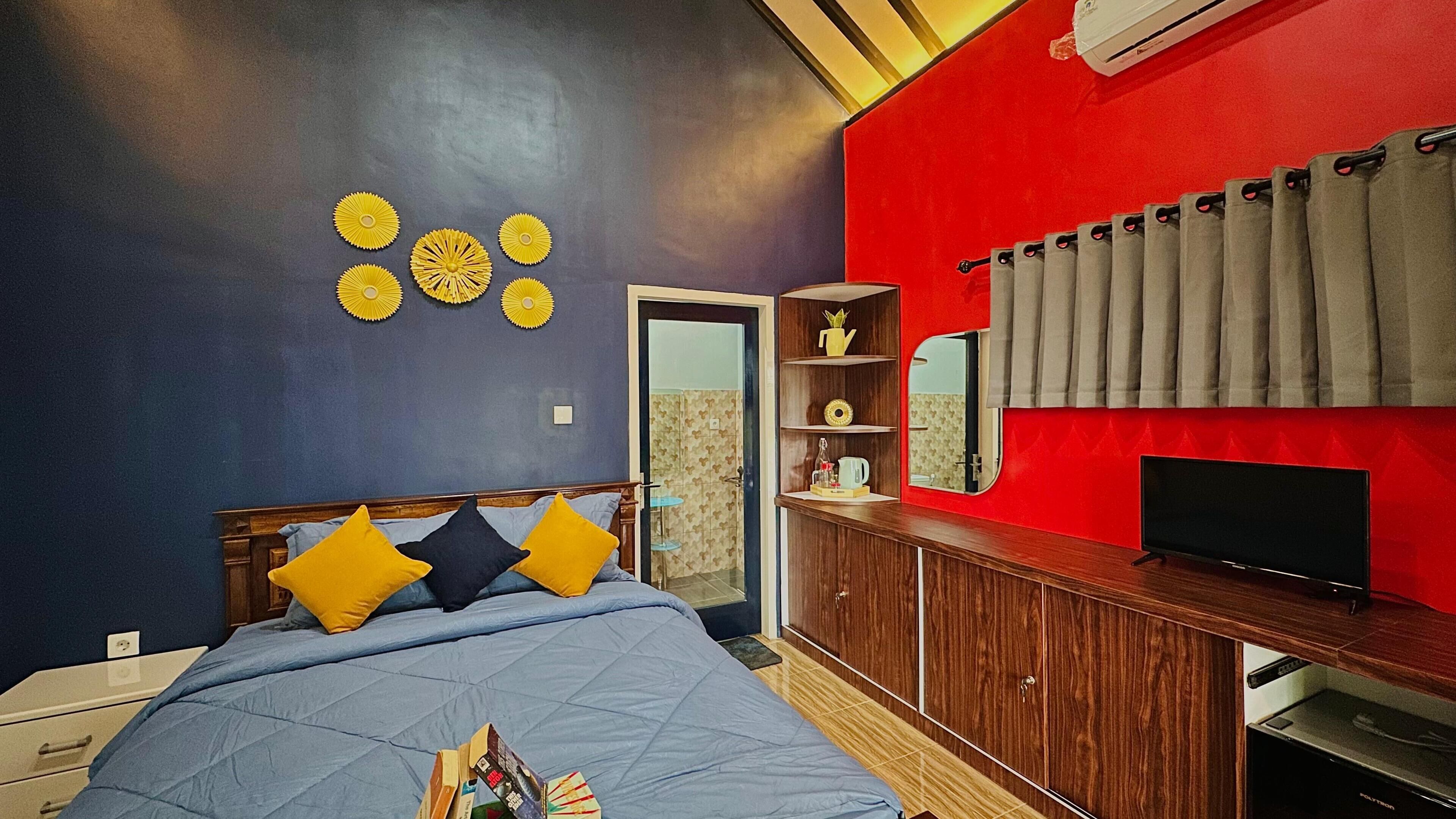 A bedroom with a bed, a TV, a wardrobe, and a red accent wall.