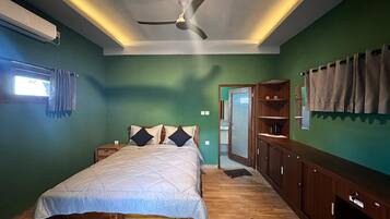 Une chambre à coucher comprenant un lit, des tables de chevet, une armoire, un ventilateur de plafond et une fenêtre avec des rideaux.