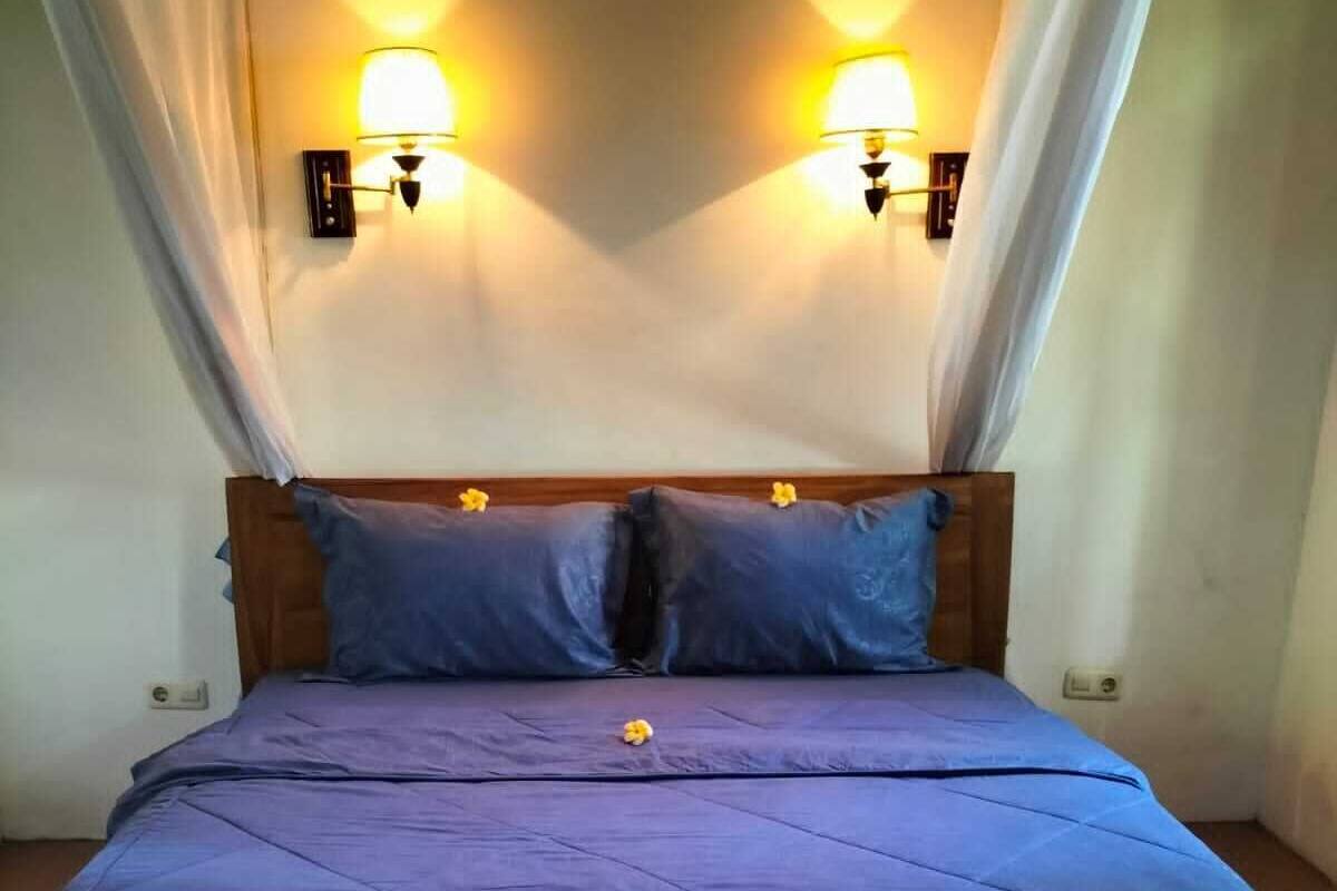 A bed with a blue quilt, two pillows, and a wooden headboard.