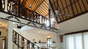 A spacious dining area with a large table and chairs, a kitchen in the background, and a staircase with ornate railings. - Villa Kamila Senggigi By Villaloka (Senggigi)