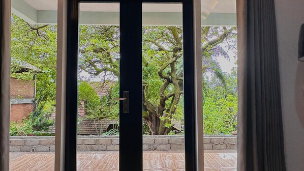 A view through a glass door to an outdoor area with a brick wall, a tiled patio, and a large tree.