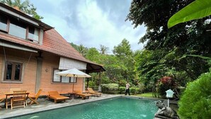 A swimming pool with a tiled deck, surrounded by lush greenery and a house with a tiled roof. - Villa Kamila Senggigi By Villaloka (Senggigi)