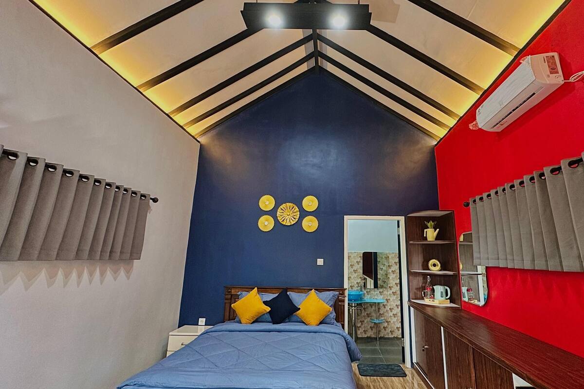 A bedroom with a bed, a red wall, and a ceiling with a unique design.