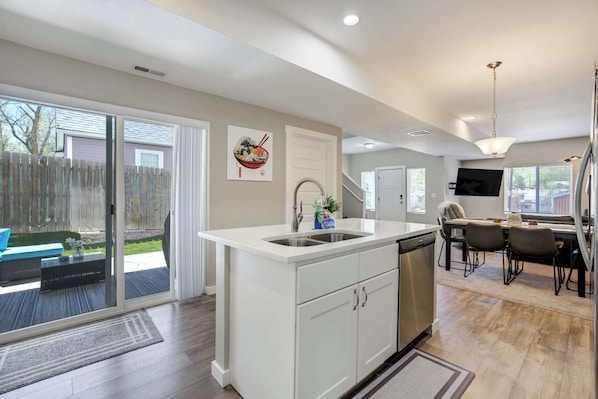A modern kitchen with a dishwasher, a dining area with a table and chairs, and a sliding glass door leading to a patio.