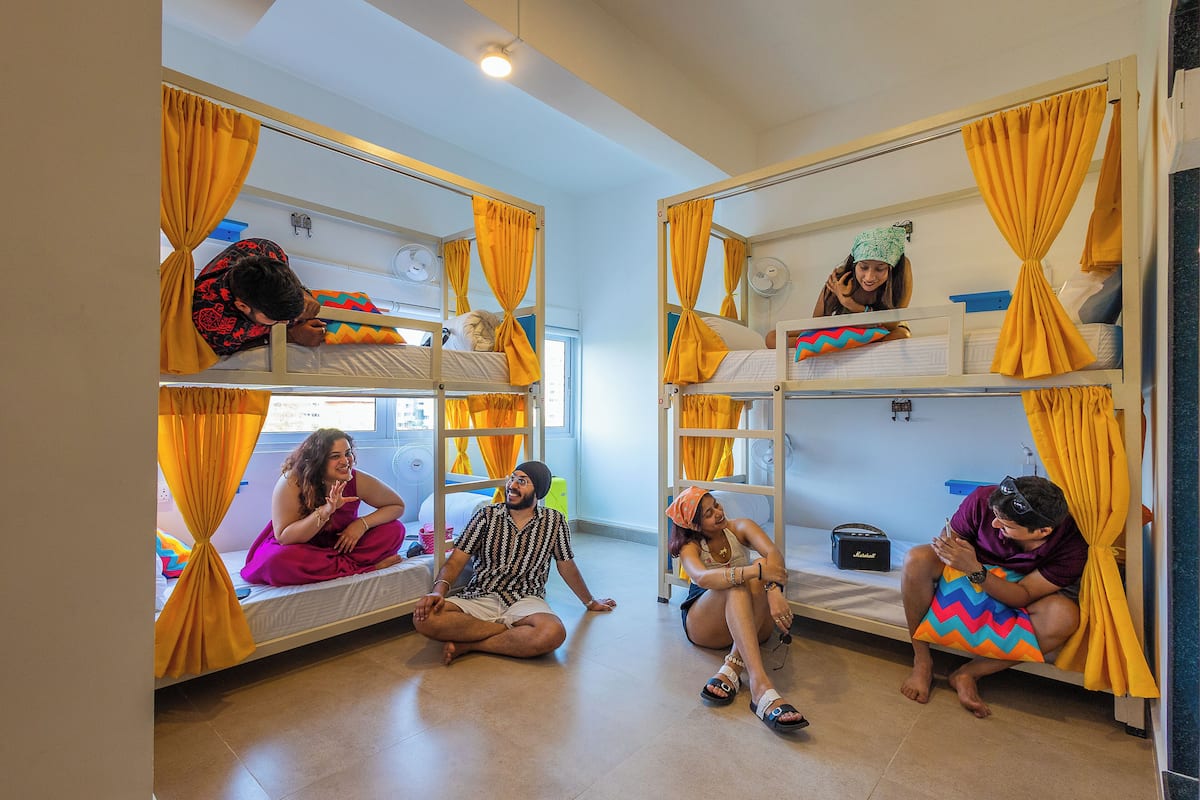 Um quarto tipo dormitório com beliches, cortinas amarelas e um pequeno ventilador no beliche superior.