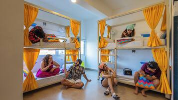 A dormitory room with bunk beds, yellow curtains, and a small fan on the upper bunk.