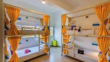 A dormitory room with bunk beds, curtains, a suitcase, and a fan.