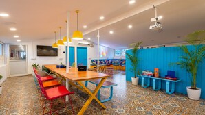 Ein modernes Interieur mit einem Holztisch, bunten Stühlen, einem Projektor und einer blauen Raumtrennung.