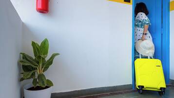 A hallway with a fire extinguisher, a potted plant, a bright yellow suitcase, and a door with a blue frame.