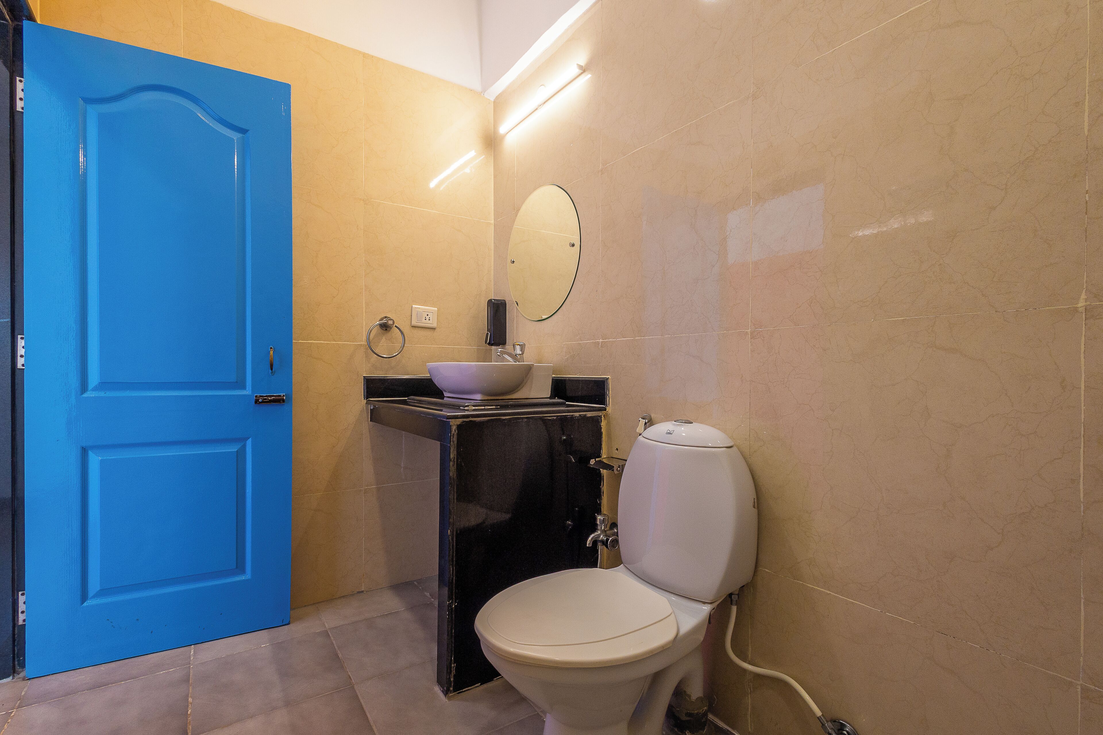Un baño con una puerta azul, un inodoro blanco, un lavabo negro y un espejo.