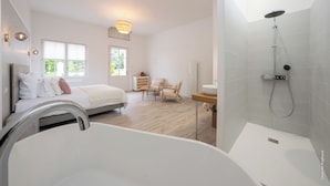 Een moderne slaapkamer met een groot bed, een nachtkastje, een stoel, een bureau en een douche.