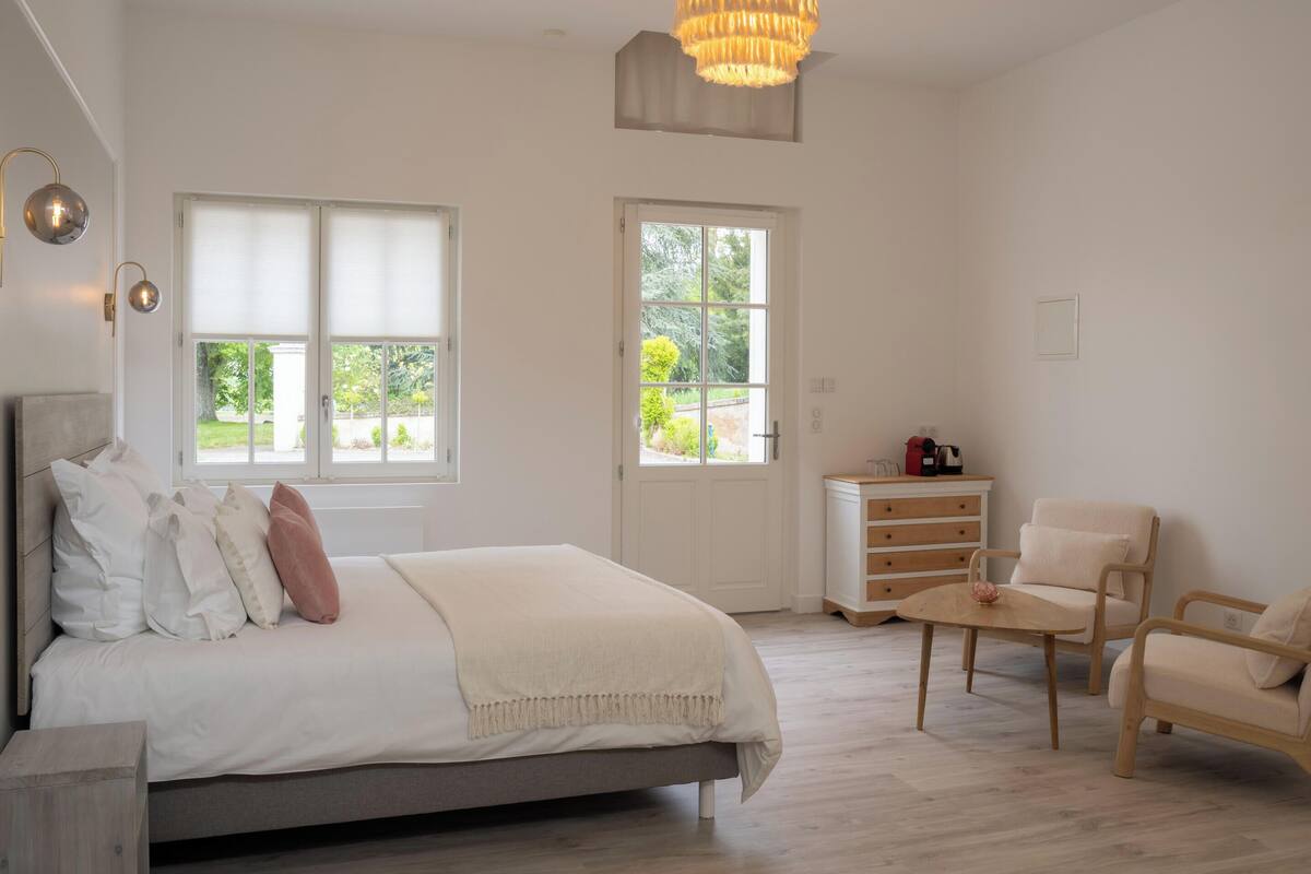 Een slaapkamer met een bed, twee ramen, een deur, een dressoir, een stoel en een tafel.