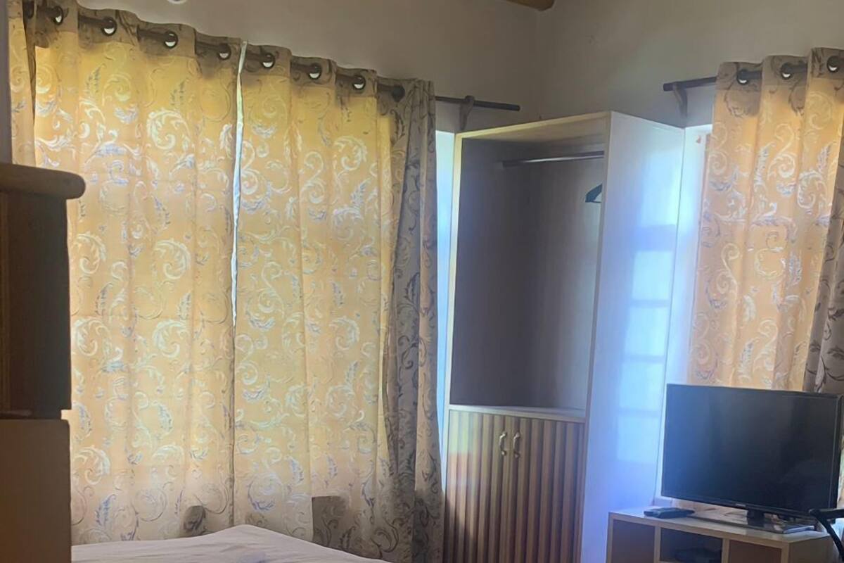 A bedroom with a bed, a TV, a wardrobe, and a ceiling fan.