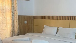 Una cama bien tendida con sábanas y almohadas blancas, un cabecero de madera y piso de madera.