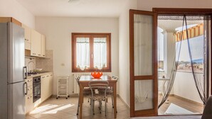 A compact kitchen with a dining table, chairs, a refrigerator, and a window with curtains.