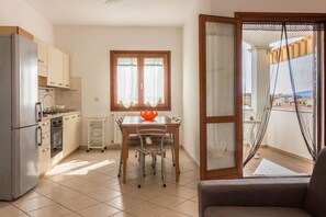 A compact kitchen with a dining table, chairs, a refrigerator, and a window with curtains.