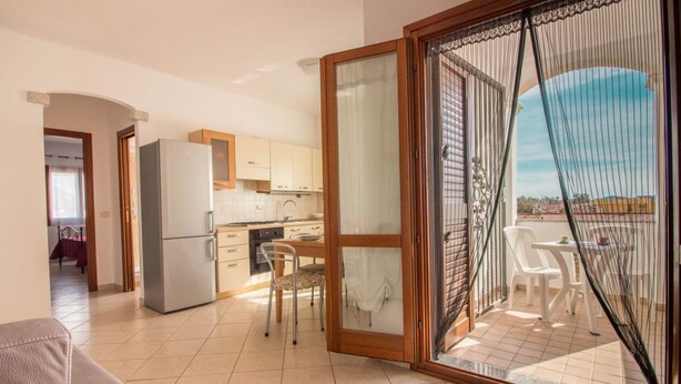 A kitchen with a refrigerator, a dining table with chairs, and a sliding glass door leading to a balcony with outdoor furniture.