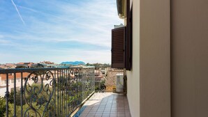 A balcony with a metal railing, a tiled floor, and a view of buildings and mountains.