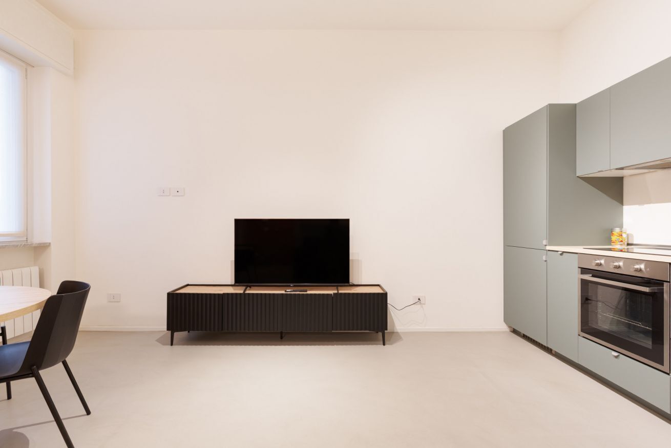 Une cuisine moderne dotée d’un four encastré, d’un coin repas avec une table et des chaises, et d’un téléviseur à écran plat fixé à un meuble.