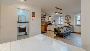 Ein modernes Hotelzimmer mit Bett, Sofa, Küchenzeile und Esstisch.