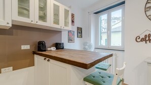 Eine Küche mit weißen Schränken, einer Holz Arbeitsplatte, einem grün gepolsterten Stuhl und einem Fenster mit Blick.