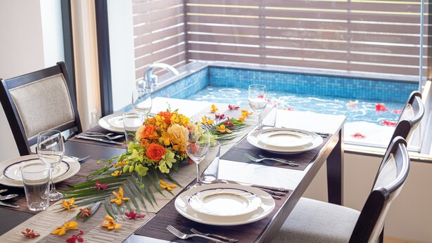 Une table à manger dressée pour quatre personnes, avec vue sur une piscine.