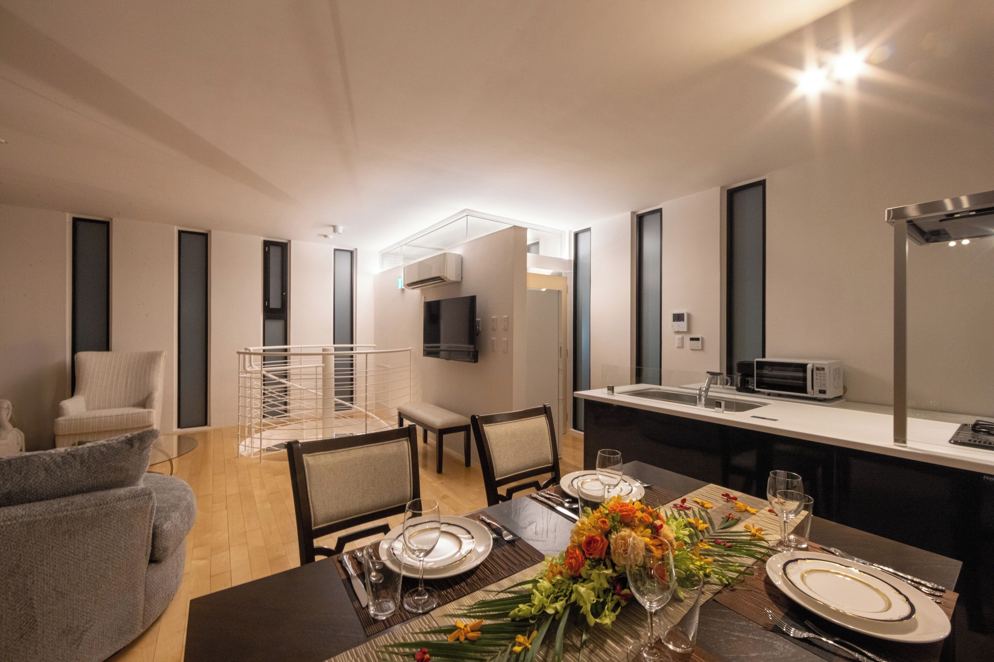 A modern dining area with a table set for four, a sofa, and a TV in the background.
