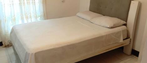 A single-bed room with a plain white bedspread, a headboard, and a small bedside table.