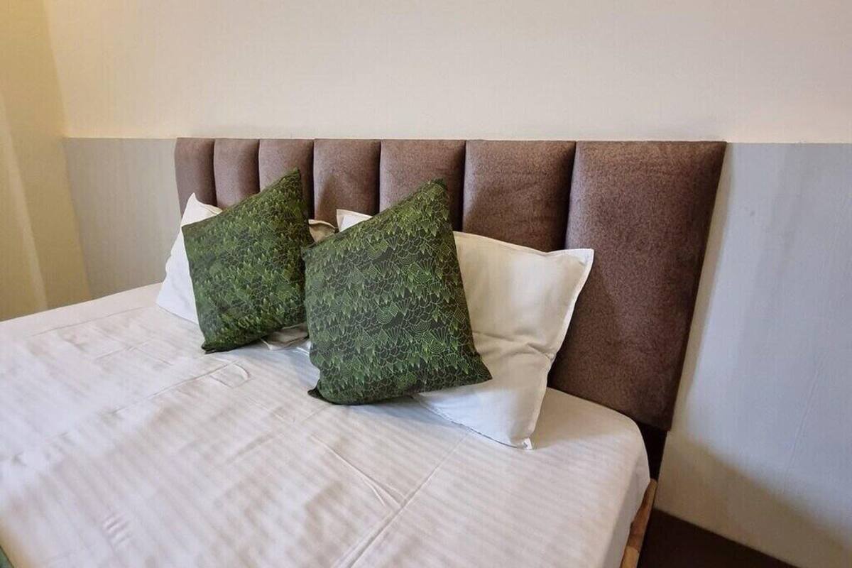 Un lit bien fait, avec une tête de lit marron et deux coussins verts à motifs.