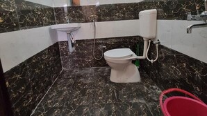 Een badkamer met een toilet, wastafel en een rode emmer.
