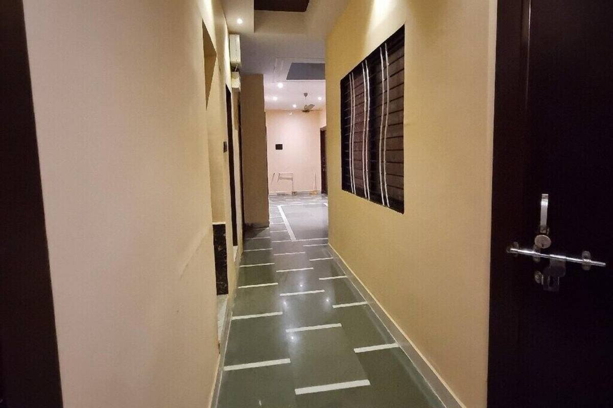 Un couloir avec un sol à rayures vertes et blanches, des murs de couleur beige et une porte sombre sur le côté droit.
