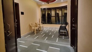 Een hal met een rood plafond, beige muren en een vloer met een patroon. Aan weerszijden bevinden zich twee deuren, een plafondventilator en een raam met jaloezieën.