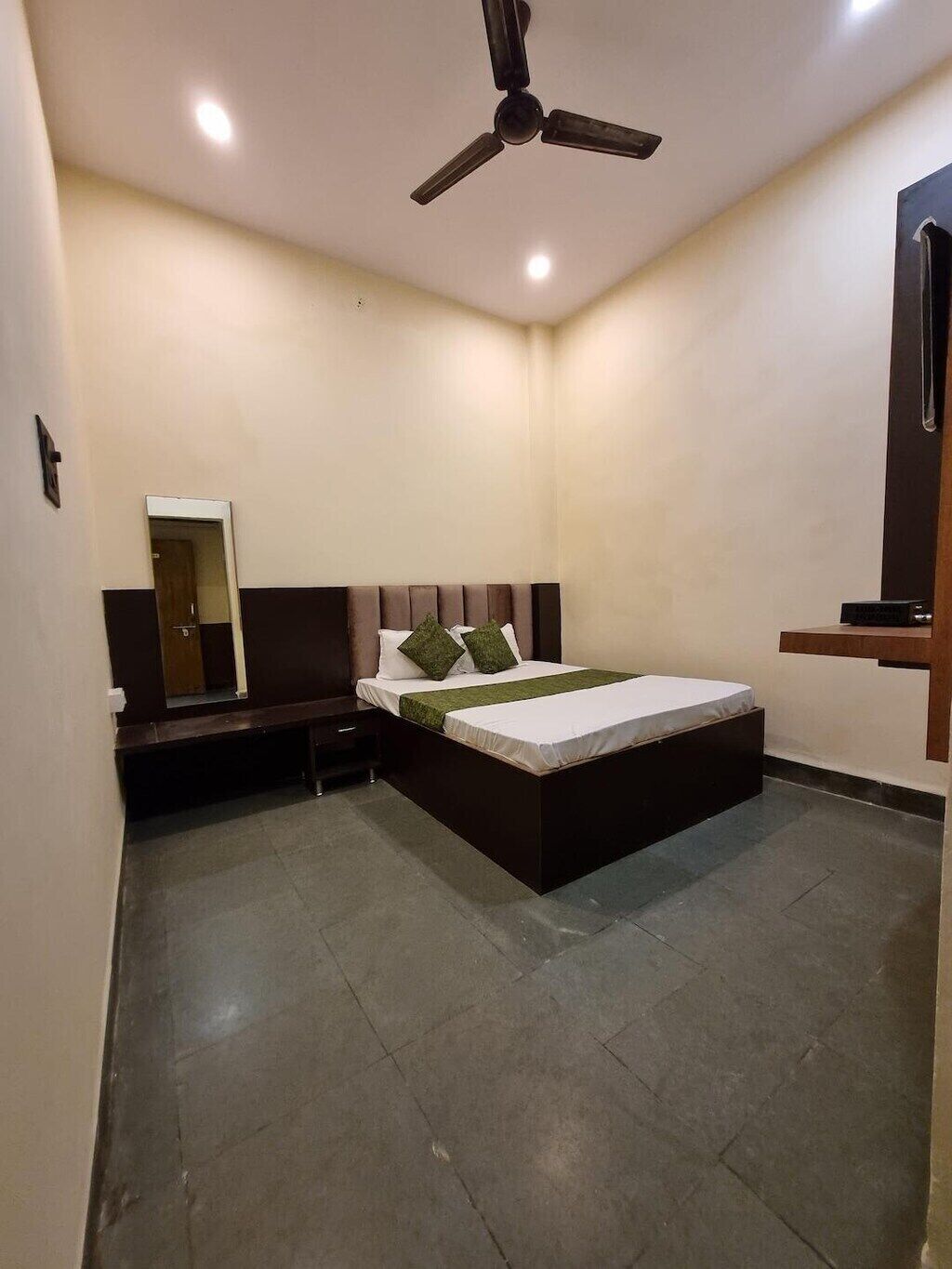 A bedroom with a bed, a nightstand, a mirror, a ceiling fan, and a TV.