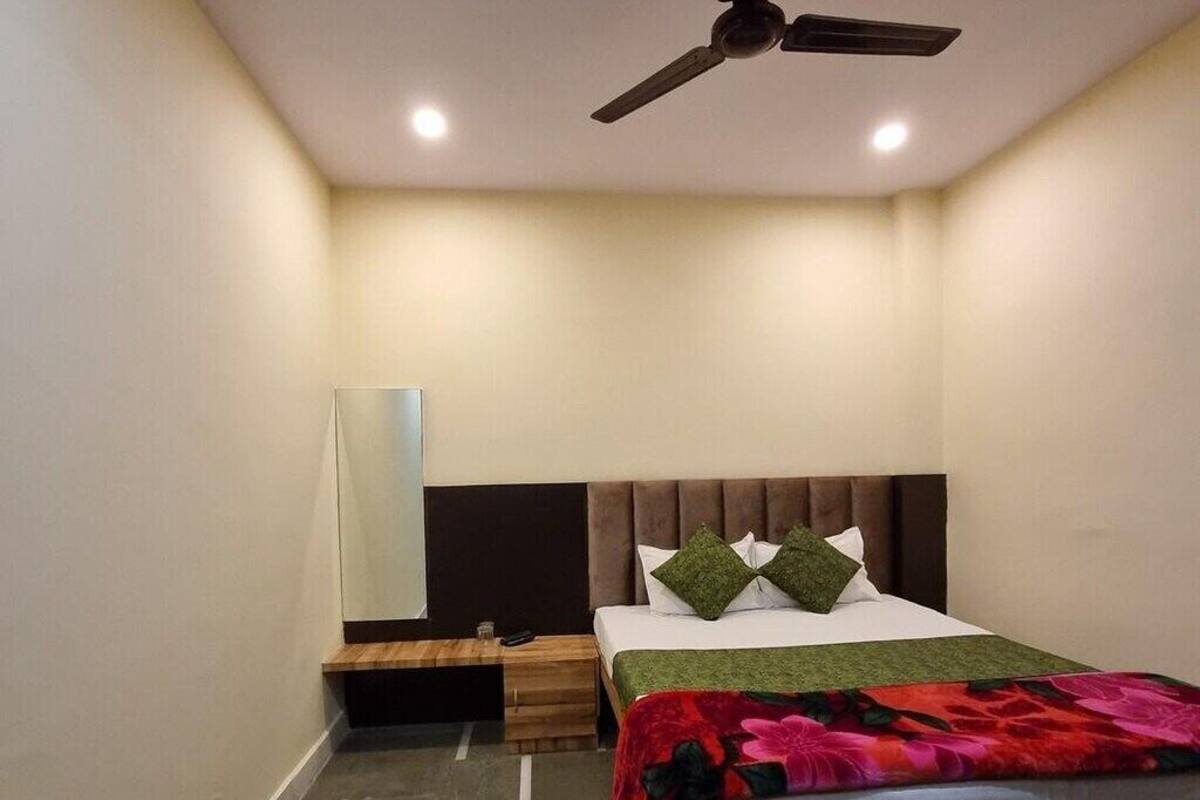 Une chambre à coucher comprenant un lit, une table de chevet, un ventilateur de plafond et un téléviseur fixé au mur.