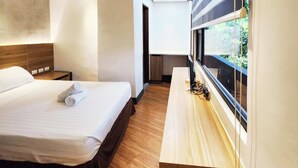 A modern hotel room with a neatly made bed, a wooden nightstand, and a window with a view of greenery. - Boulevard Pension Hotel powered by Cocotel (Cebu City)