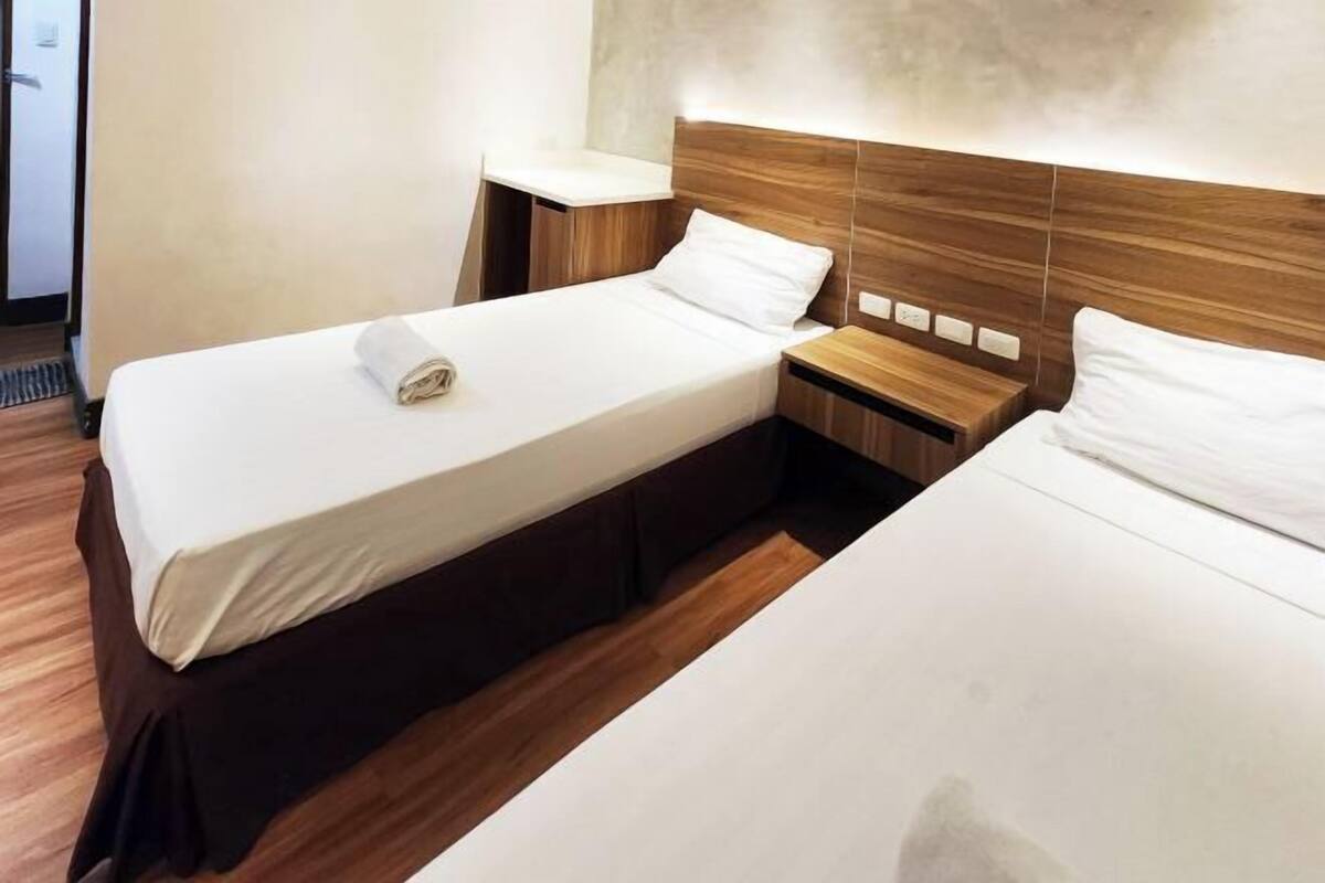 Habitación de hotel con dos camas, cabecera de madera, mesita de noche y lámpara de pared.