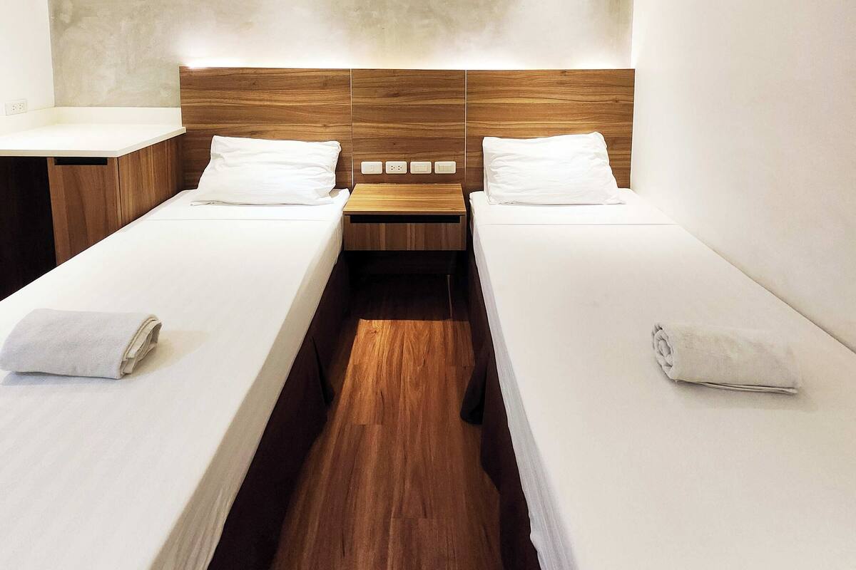 Una habitación de hotel con dos camas individuales, cabeceros de madera, ropa de cama blanca y una mesita de noche de madera entre las camas.