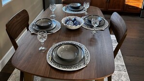 Un coin repas avec une table en bois, dressée pour quatre personnes, et équipé d’une machine à café intégrée, d’un réfrigérateur et de placards en bois.